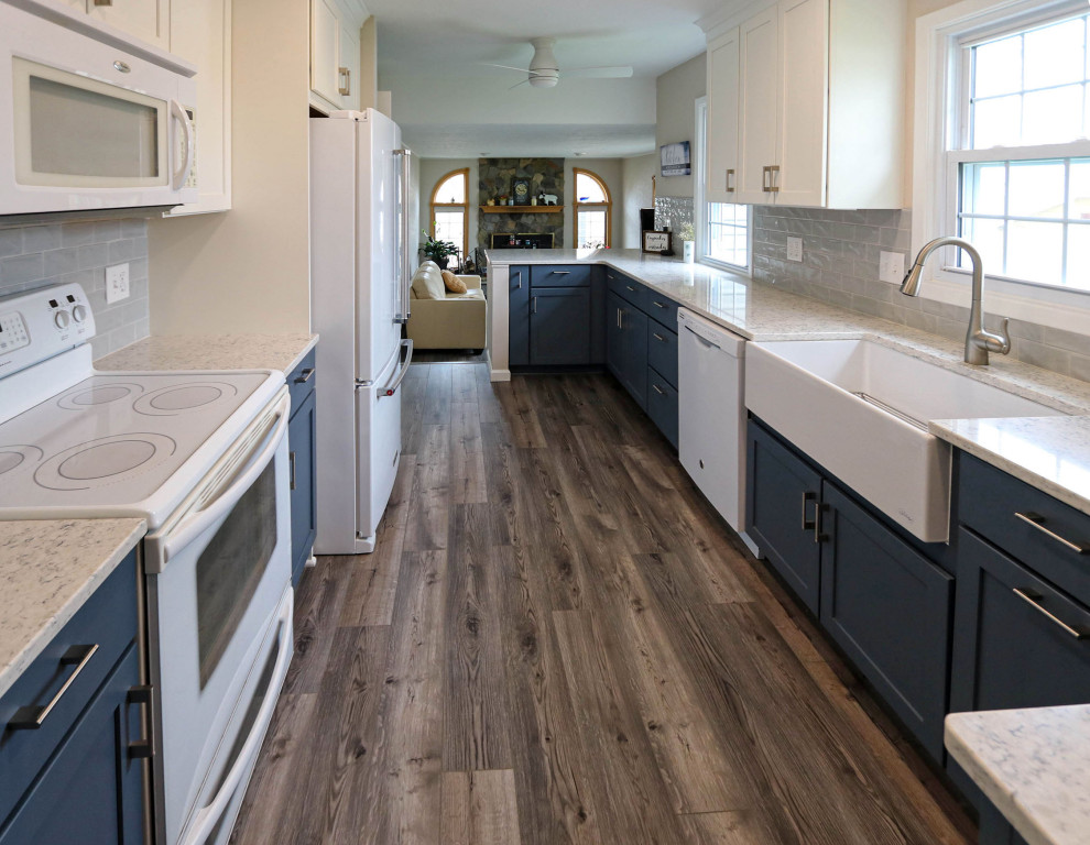 Mid-sized transitional galley kitchen pantry in Cleveland with a farmhouse sink, flat-panel cabinets, blue cabinets, quartz benchtops, grey splashback, ceramic splashback, white appliances, porcelain floors, no island, brown floor and white benchtop.