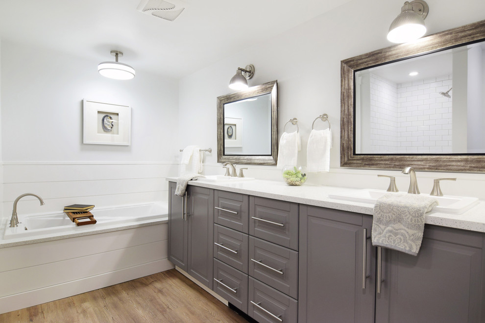 This is an example of a large traditional master bathroom in Vancouver with raised-panel cabinets, grey cabinets, an alcove tub, an alcove shower, a two-piece toilet, white tile, subway tile, white walls, vinyl floors, a drop-in sink, engineered quartz benchtops, brown floor, a hinged shower door and white benchtops.
