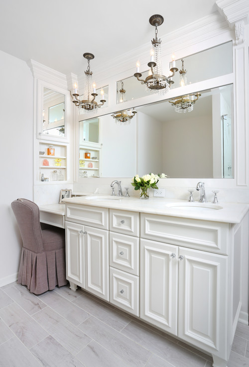 White bathroom with double-sink vanity of raised-panel RTA cabinets, crown molding, quartz top, large mirror, and vintage chandeliers beside a makeup nook.