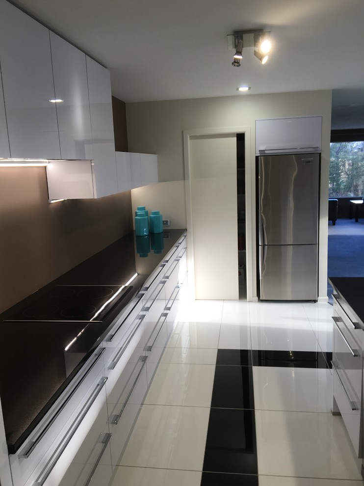 This is an example of a medium sized contemporary l-shaped kitchen pantry in Christchurch with a submerged sink, white cabinets, granite worktops, brown splashback, stainless steel appliances, porcelain flooring, an island and yellow floors.