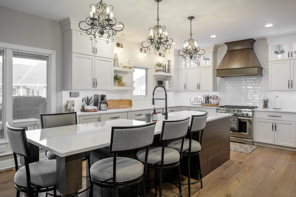 Eat-in kitchen - u-shaped brown floor eat-in kitchen idea with shaker cabinets, white cabinets, quartz countertops, white backsplash, subway tile backsplash, stainless steel appliances, an island, white countertops and a farmhouse sink
