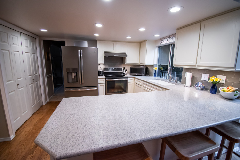 Inspiration for a transitional u-shaped medium tone wood floor open concept kitchen remodel in Seattle with an undermount sink, shaker cabinets, white cabinets, quartz countertops, gray backsplash, glass tile backsplash, stainless steel appliances, a peninsula and multicolored countertops