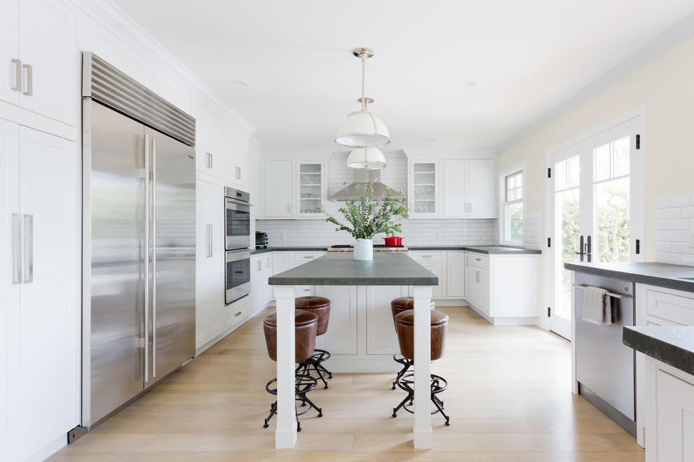 Photo of a transitional u-shaped kitchen in Los Angeles with shaker cabinets, white cabinets, white splashback, subway tile splashback, stainless steel appliances, light hardwood floors, with island and beige floor.