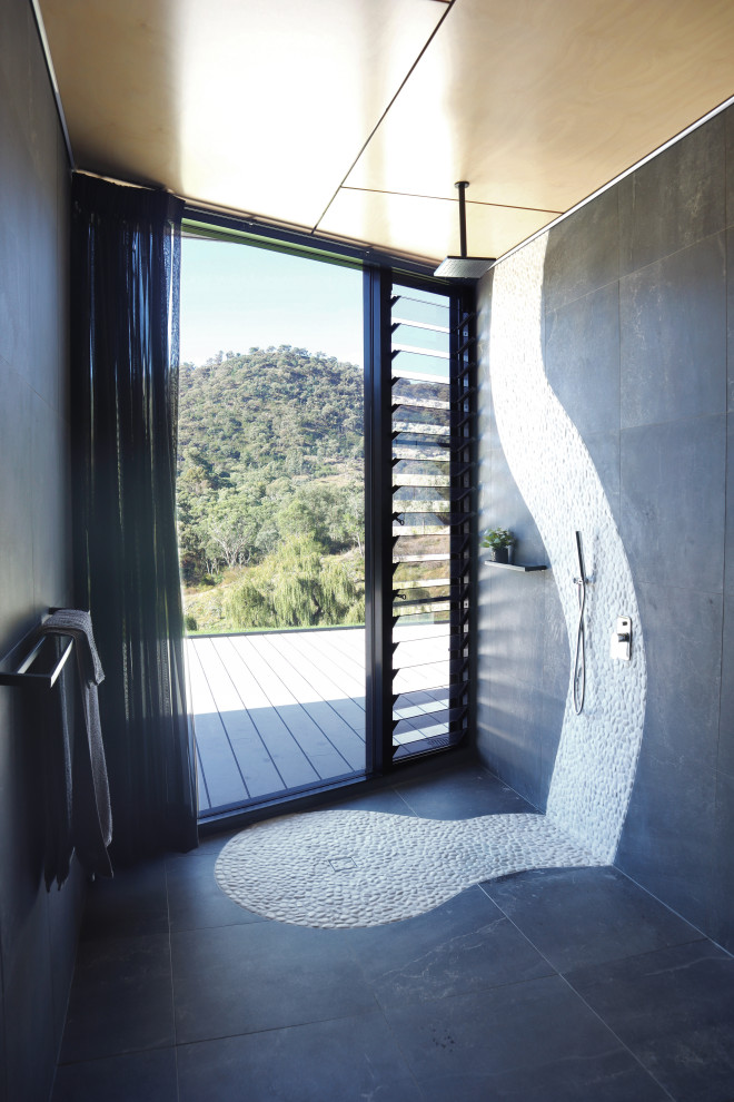 Inspiration for a large contemporary master bathroom in Wollongong with a freestanding tub, an open shower, a wall-mount toilet, black tile, ceramic tile, black walls, ceramic floors, black floor, an open shower and timber.