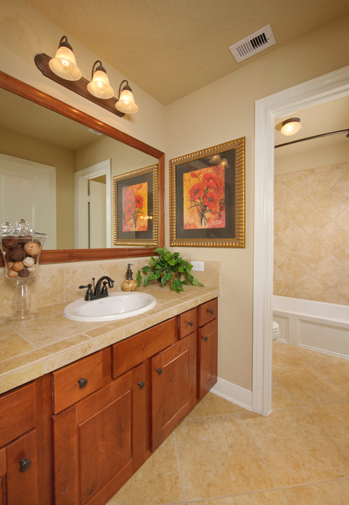 This is an example of a mid-sized traditional kids bathroom in Houston with raised-panel cabinets, dark wood cabinets, an alcove tub, a shower/bathtub combo, a two-piece toilet, beige tile, porcelain tile, beige walls, porcelain floors, a drop-in sink, tile benchtops, beige floor, a shower curtain and beige benchtops.