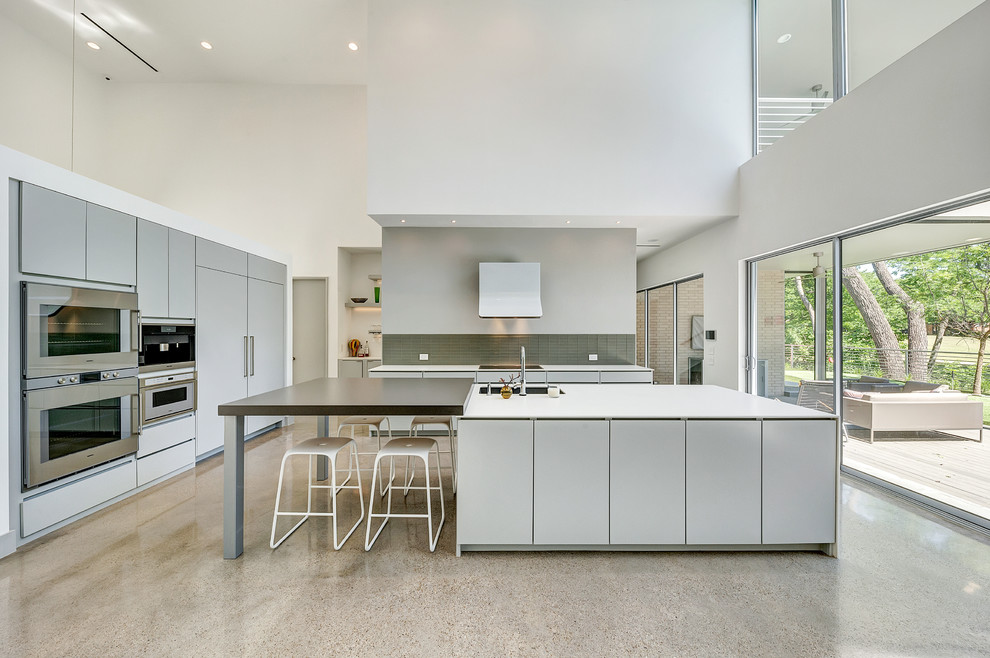 Large contemporary kitchen in Dallas with flat-panel cabinets, grey cabinets, quartzite benchtops, grey splashback, glass tile splashback, stainless steel appliances, concrete floors, grey floor, an undermount sink and multiple islands.