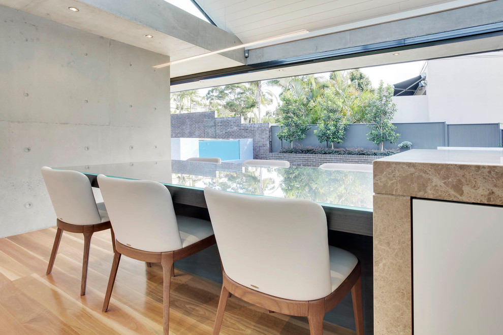 Photo of an expansive modern l-shaped eat-in kitchen in Sydney with an undermount sink, flat-panel cabinets, beige cabinets, marble benchtops, grey splashback, glass sheet splashback, black appliances, medium hardwood floors and with island.