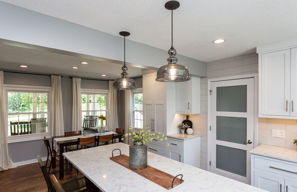 Example of a large transitional l-shaped medium tone wood floor and brown floor eat-in kitchen design with a farmhouse sink, recessed-panel cabinets, white cabinets, quartz countertops, white backsplash, ceramic backsplash, colored appliances, an island and white countertops