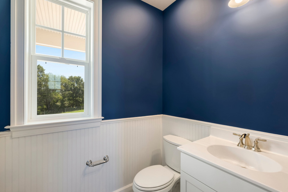 Modelo de aseo a medida de estilo de casa de campo de tamaño medio con paredes azules, suelo azul, encimeras blancas, armarios con paneles empotrados, puertas de armario blancas, suelo laminado, lavabo integrado y encimera de acrílico