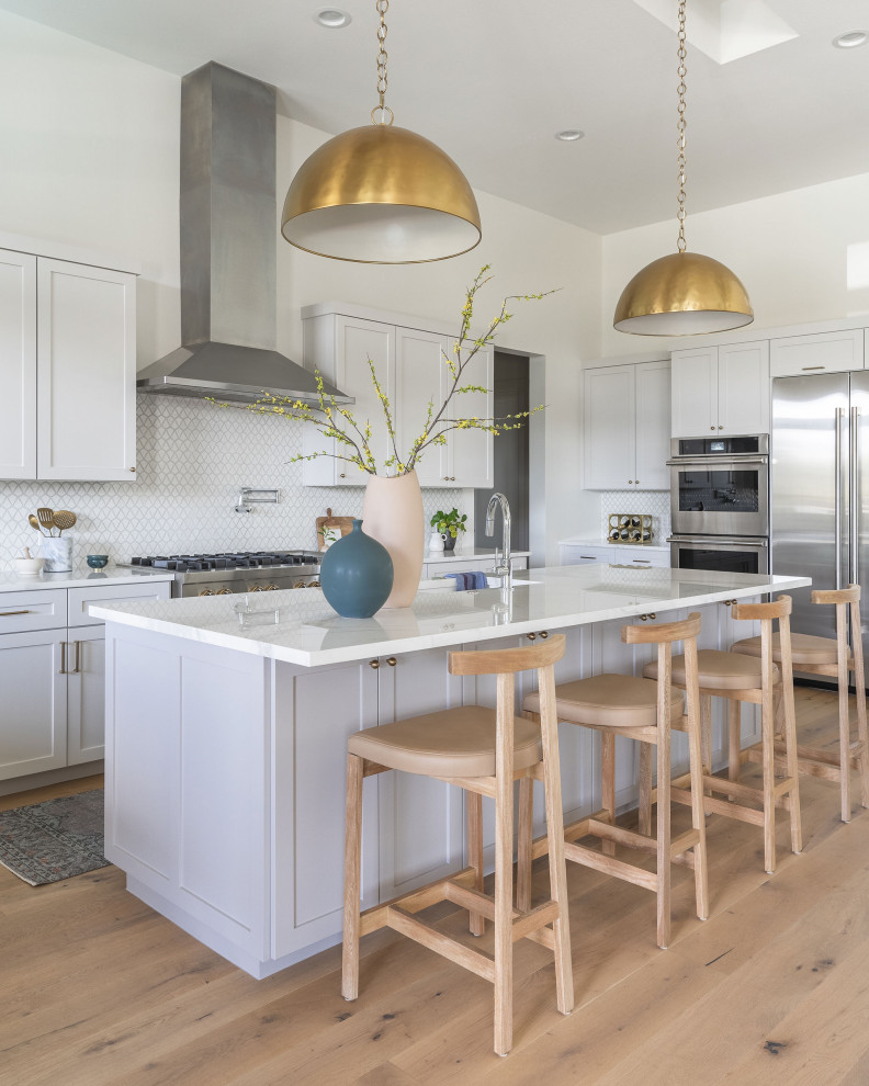 Inspiration for a transitional galley light wood floor and beige floor kitchen remodel in Austin with white cabinets, white backsplash, mosaic tile backsplash, stainless steel appliances, white countertops, shaker cabinets and an island