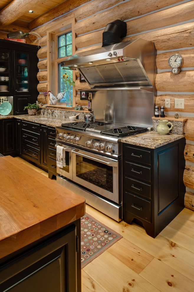 This is an example of a country l-shaped eat-in kitchen in Other with an undermount sink, raised-panel cabinets, black cabinets, wood benchtops, multi-coloured splashback, stone slab splashback and stainless steel appliances.