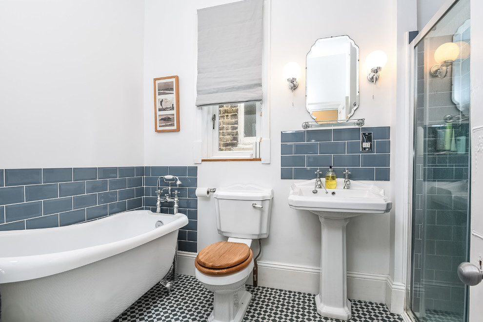 Mid-sized transitional bathroom in London with a claw-foot tub, a corner shower, a two-piece toilet, blue tile, subway tile, white walls, a pedestal sink, multi-coloured floor and a hinged shower door.