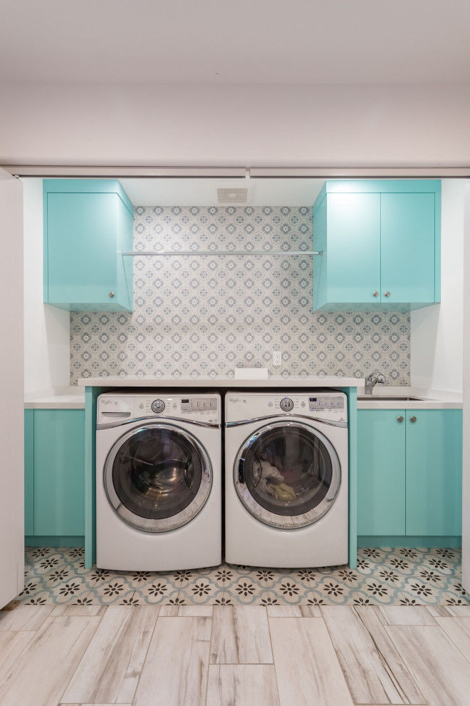 Design ideas for a small single-wall laundry cupboard in Los Angeles with a drop-in sink, flat-panel cabinets, turquoise cabinets, wood benchtops, multi-coloured splashback, ceramic splashback, white walls, ceramic floors, a side-by-side washer and dryer, multi-coloured floor, white benchtop, vaulted and panelled walls.