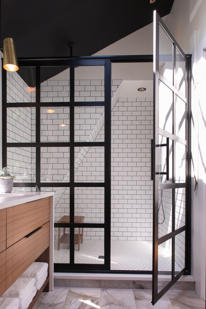This is an example of a mid-sized transitional master bathroom in Philadelphia with flat-panel cabinets, medium wood cabinets, a corner shower, a one-piece toilet, white tile, subway tile, white walls, porcelain floors, an undermount sink, engineered quartz benchtops, multi-coloured floor and a hinged shower door.
