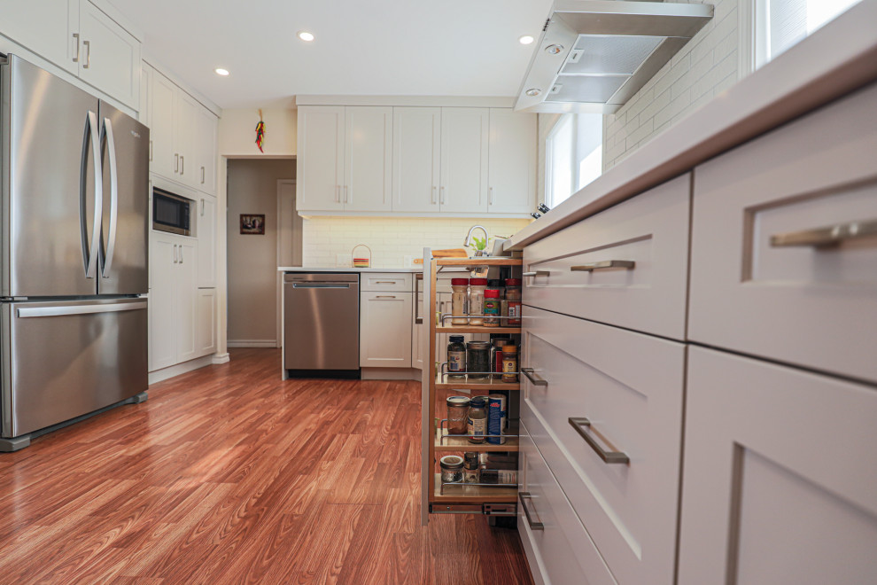 Mid-sized transitional l-shaped vinyl floor and brown floor eat-in kitchen photo in Edmonton with an undermount sink, shaker cabinets, beige cabinets, quartz countertops, white backsplash, ceramic backsplash, stainless steel appliances, no island and white countertops