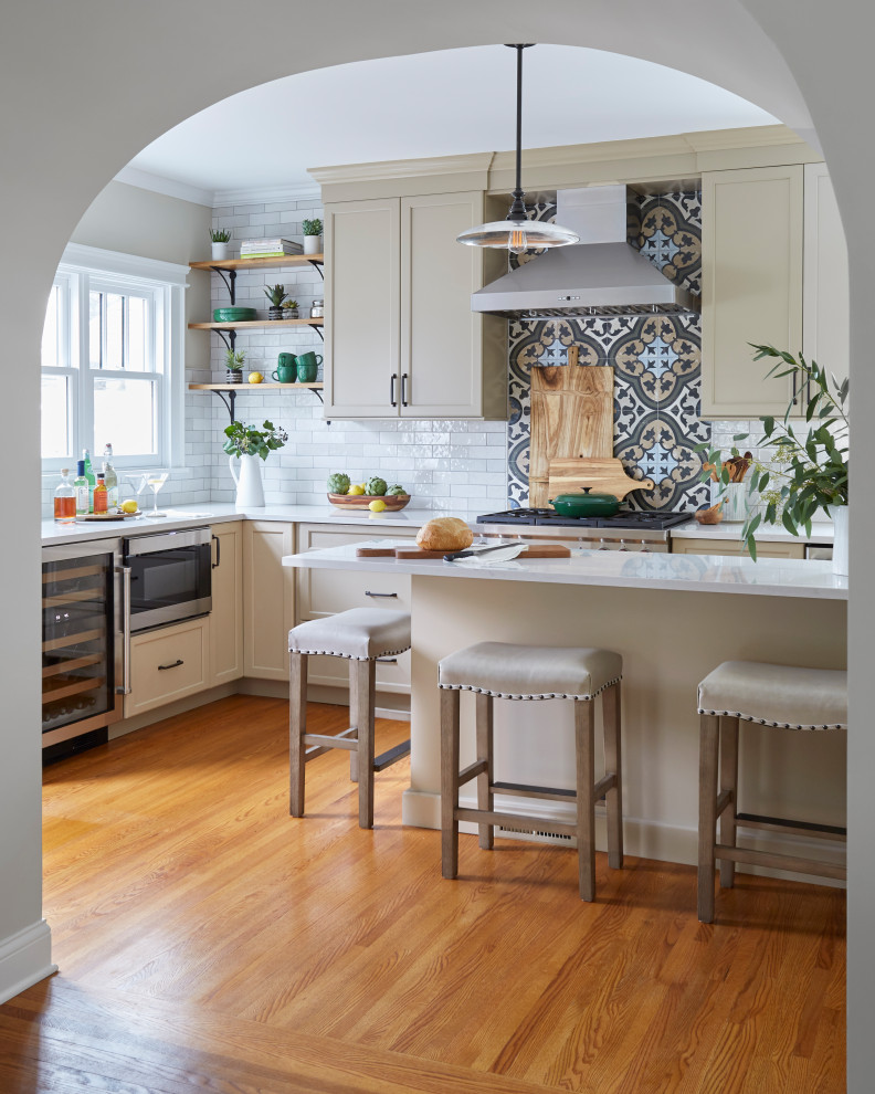 This is an example of a large traditional u-shaped eat-in kitchen in Chicago with a farmhouse sink, shaker cabinets, beige cabinets, quartzite benchtops, multi-coloured splashback, porcelain splashback, stainless steel appliances, medium hardwood floors, with island, beige benchtop and brown floor.