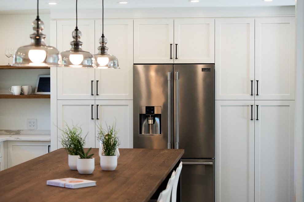 This is an example of a large contemporary l-shaped eat-in kitchen in Montreal with a farmhouse sink, shaker cabinets, brown cabinets, wood benchtops, white splashback, porcelain splashback, stainless steel appliances, porcelain floors, with island, beige floor and white benchtop.