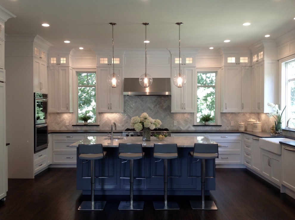 This is an example of a transitional u-shaped open plan kitchen in New York with a farmhouse sink, shaker cabinets, white cabinets, quartzite benchtops, white splashback, stone tile splashback, panelled appliances, dark hardwood floors and with island.