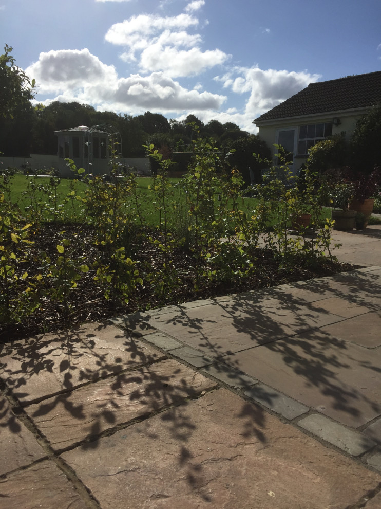 На фото: солнечный, летний регулярный сад среднего размера на заднем дворе в стиле неоклассика (современная классика) с хорошей освещенностью и покрытием из каменной брусчатки