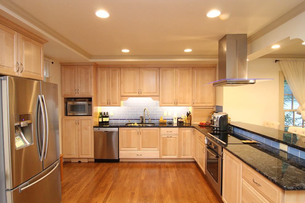 Huge transitional l-shaped medium tone wood floor open concept kitchen photo with an undermount sink, raised-panel cabinets, light wood cabinets, granite countertops, blue backsplash, glass tile backsplash and stainless steel appliances