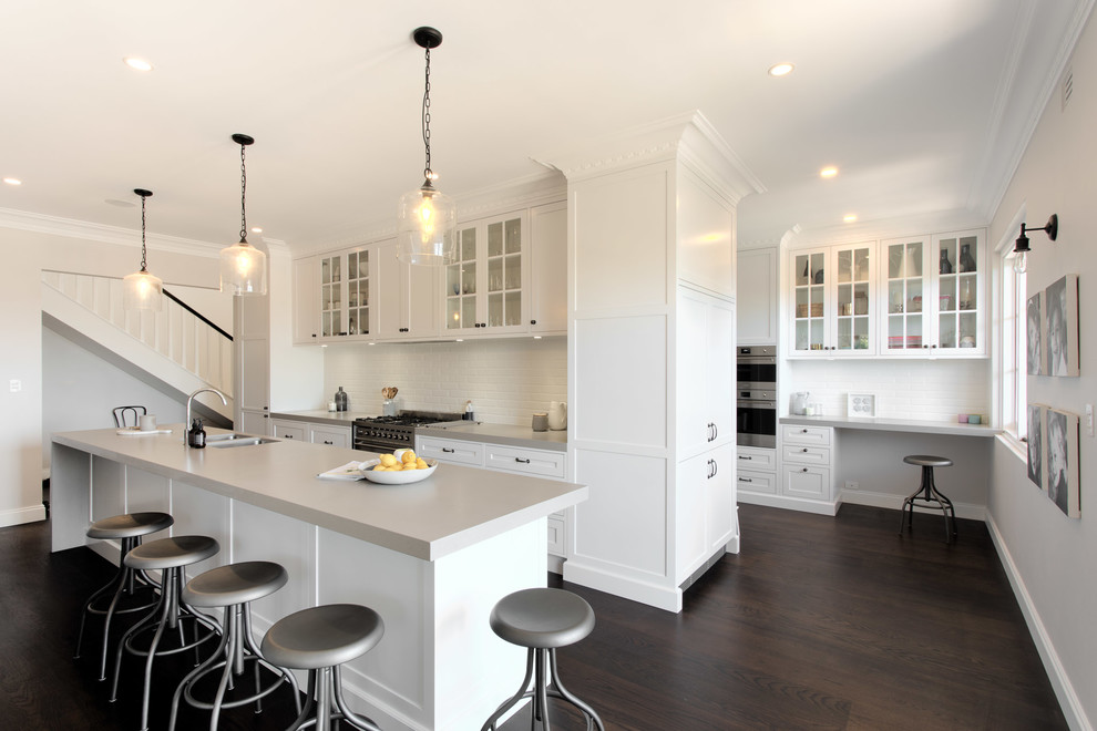 Inspiration for a large beach style galley open plan kitchen in Sydney with a double-bowl sink, flat-panel cabinets, white cabinets, white splashback, subway tile splashback, stainless steel appliances, dark hardwood floors and with island.