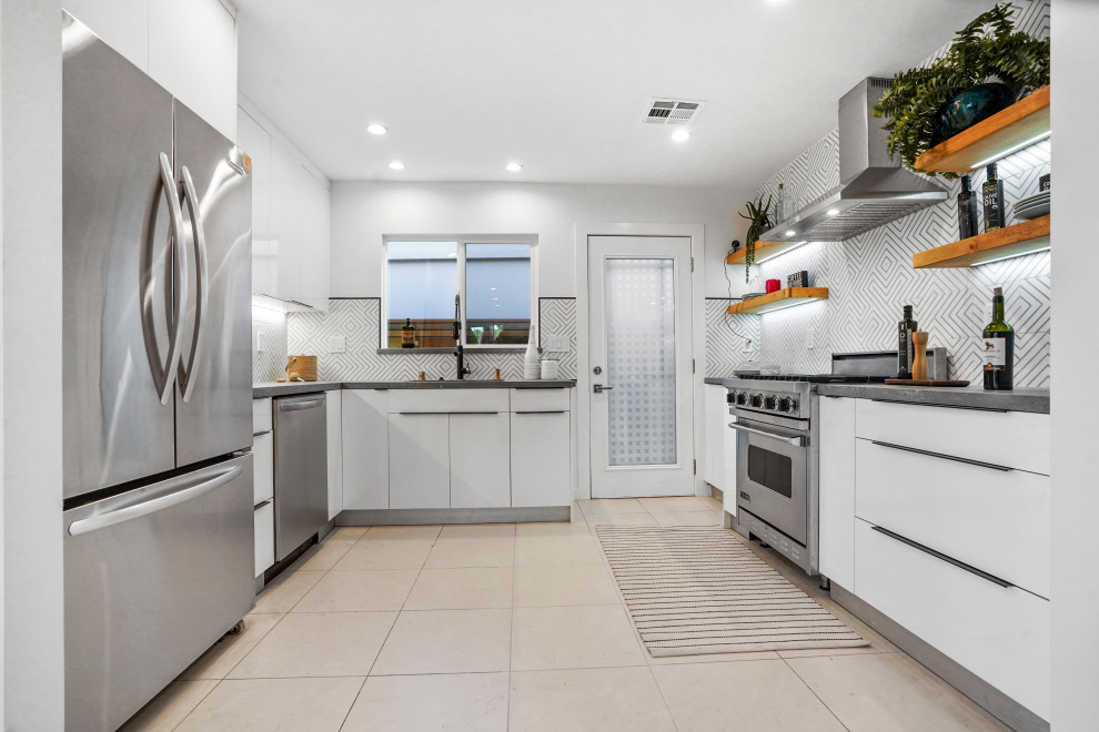 This is an example of a small contemporary u-shaped separate kitchen in Los Angeles with an undermount sink, flat-panel cabinets, white cabinets, quartz benchtops, white splashback, cement tile splashback, stainless steel appliances, porcelain floors, beige floor and grey benchtop.