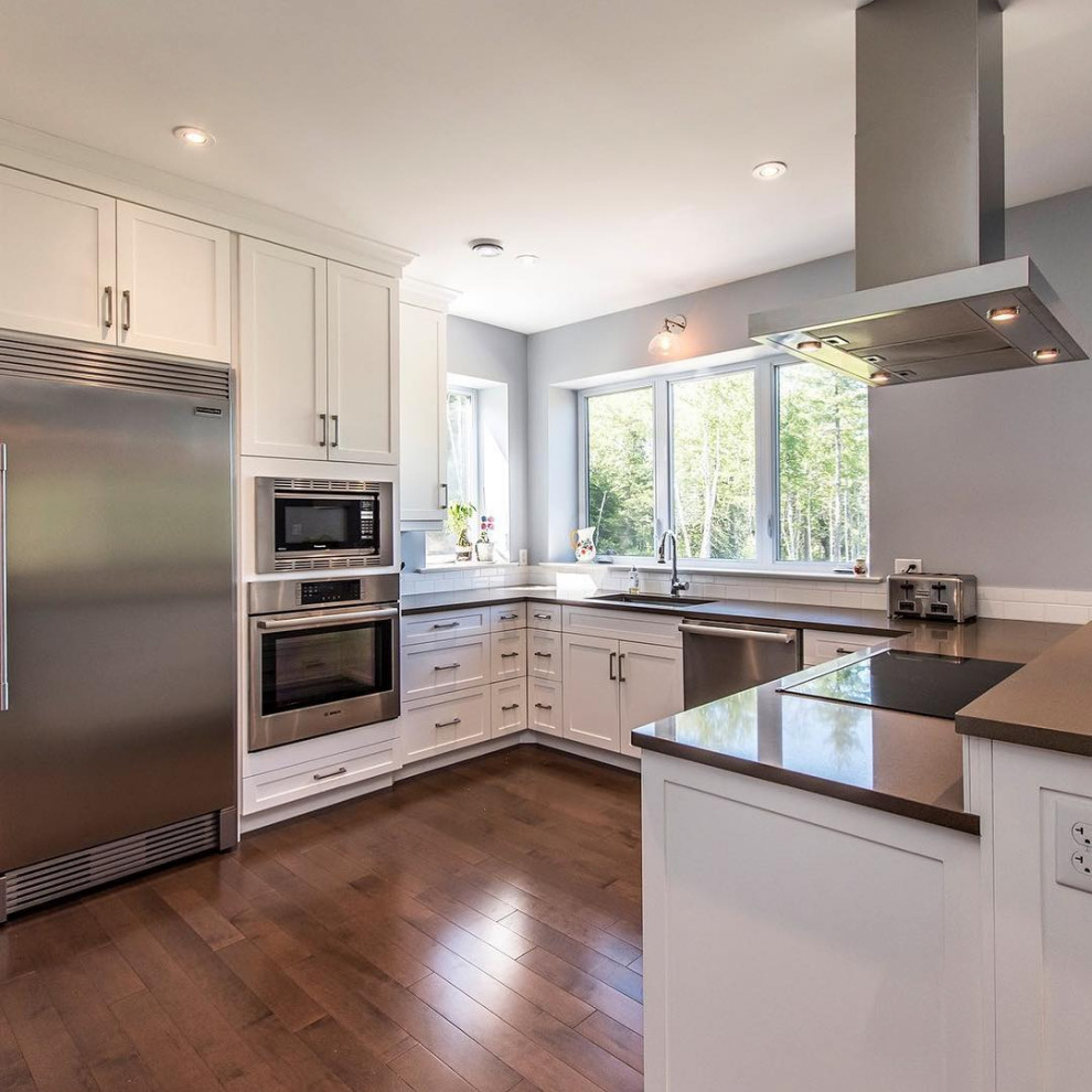 Mid-sized u-shaped medium tone wood floor and brown floor kitchen photo with an undermount sink, recessed-panel cabinets, white cabinets, quartzite countertops, white backsplash, subway tile backsplash, stainless steel appliances, no island and black countertops