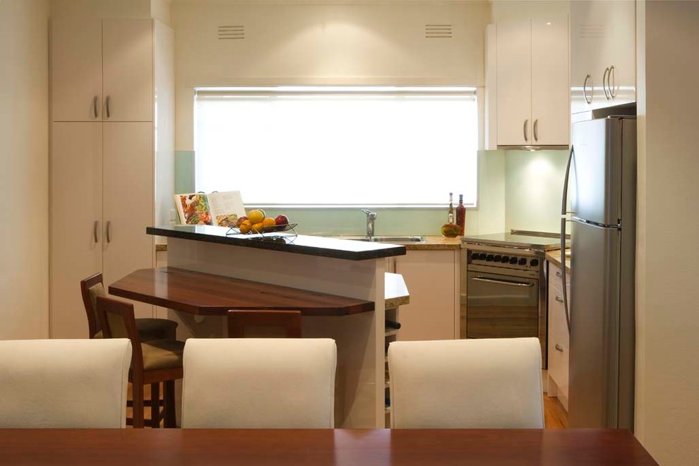 Design ideas for a mid-sized modern l-shaped eat-in kitchen in Melbourne with with island, flat-panel cabinets, white cabinets, wood benchtops, green splashback, glass sheet splashback, stainless steel appliances, a double-bowl sink and light hardwood floors.
