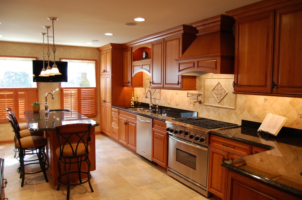 Inspiration for a large traditional galley eat-in kitchen in Baltimore with a double-bowl sink, raised-panel cabinets, medium wood cabinets, granite benchtops, beige splashback, travertine splashback, stainless steel appliances, travertine floors, with island, beige floor and black benchtop.