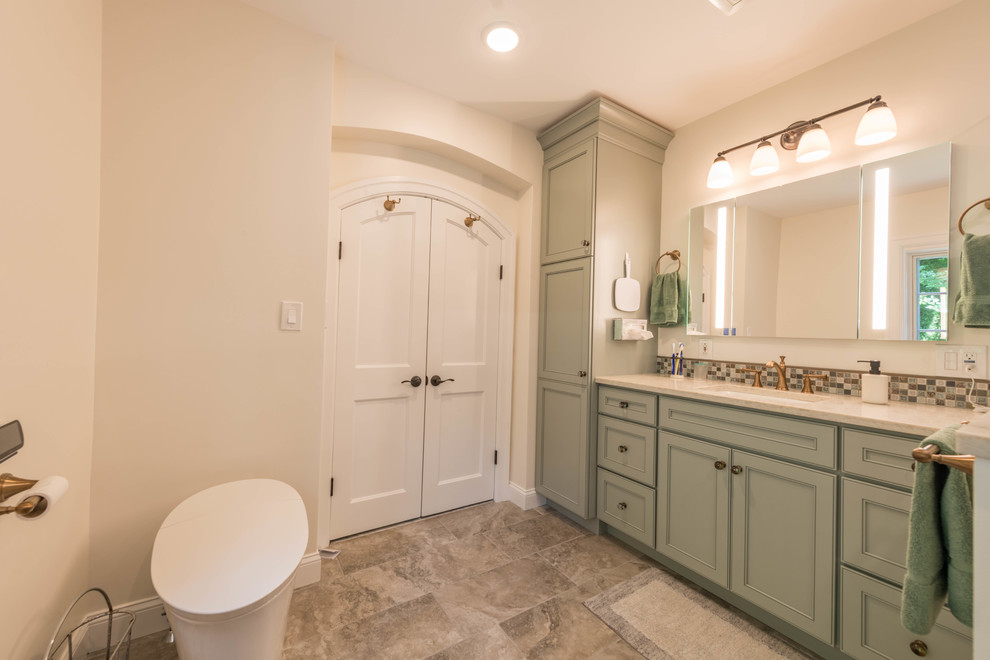 This is an example of a mid-sized traditional master bathroom in Philadelphia with furniture-like cabinets, green cabinets, a corner shower, a one-piece toilet, beige tile, marble, grey walls, porcelain floors, an undermount sink, engineered quartz benchtops, beige floor, a hinged shower door and beige benchtops.