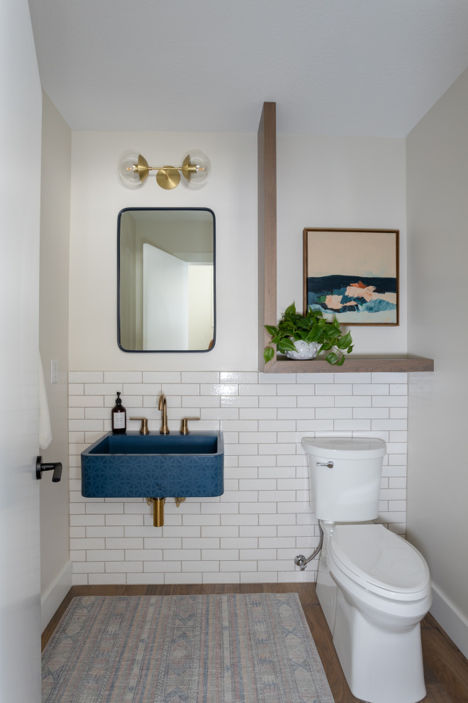 На фото: большой туалет в стиле неоклассика (современная классика) с унитазом-моноблоком, белой плиткой, плиткой кабанчик, белыми стенами, подвесной раковиной, коричневым полом и синей столешницей с