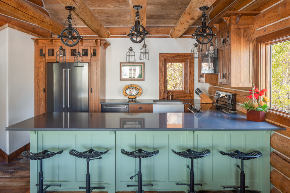 This is an example of a country u-shaped eat-in kitchen in Other with a farmhouse sink, shaker cabinets, green cabinets, brown splashback, timber splashback, stainless steel appliances, medium hardwood floors, a peninsula, brown floor and grey benchtop.
