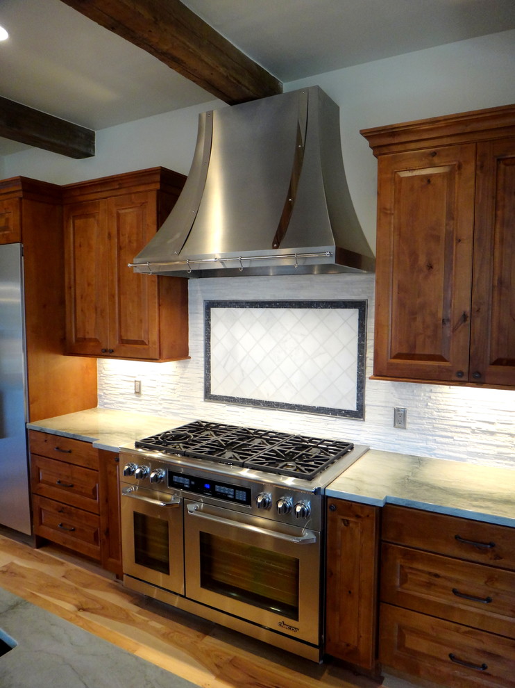 Inspiration for a mid-sized rustic l-shaped light wood floor open concept kitchen remodel in Denver with an undermount sink, raised-panel cabinets, medium tone wood cabinets, quartzite countertops, white backsplash, stone tile backsplash, stainless steel appliances, beige walls and an island