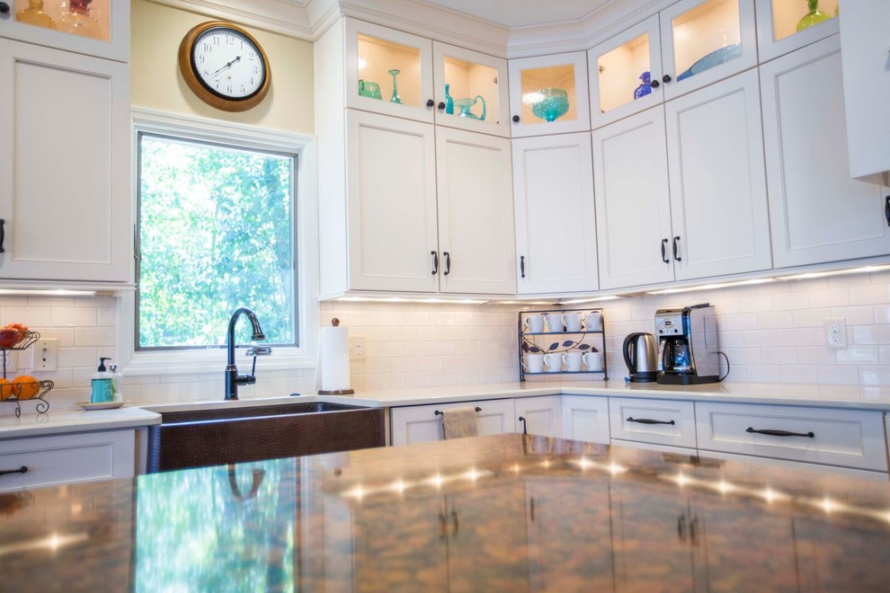 Inspiration for a large transitional l-shaped light wood floor and brown floor enclosed kitchen remodel with a farmhouse sink, shaker cabinets, white cabinets, solid surface countertops, white backsplash, porcelain backsplash, stainless steel appliances and an island