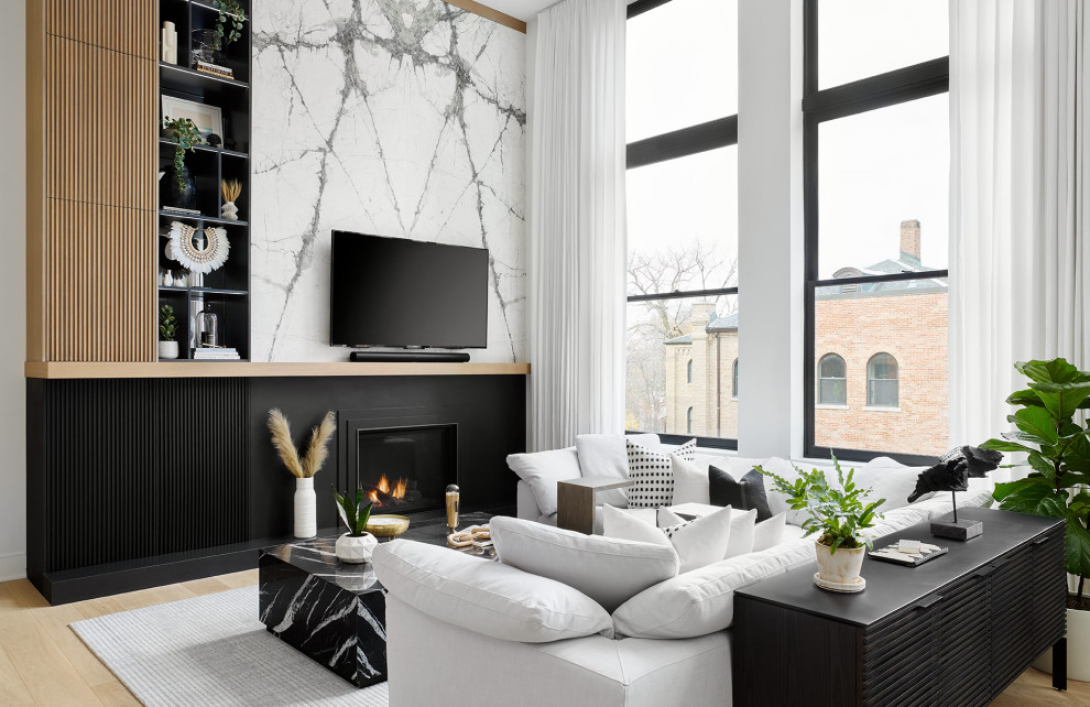 Expansive contemporary open concept living room in Chicago with white walls, light hardwood floors, a standard fireplace, a stone fireplace surround and a built-in media wall.