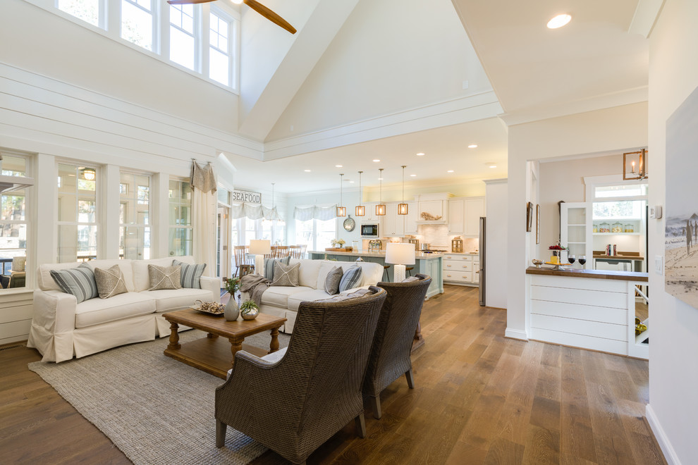 Photo of a large beach style open concept family room in Other with white walls, medium hardwood floors, a standard fireplace, a stone fireplace surround, a built-in media wall and white floor.