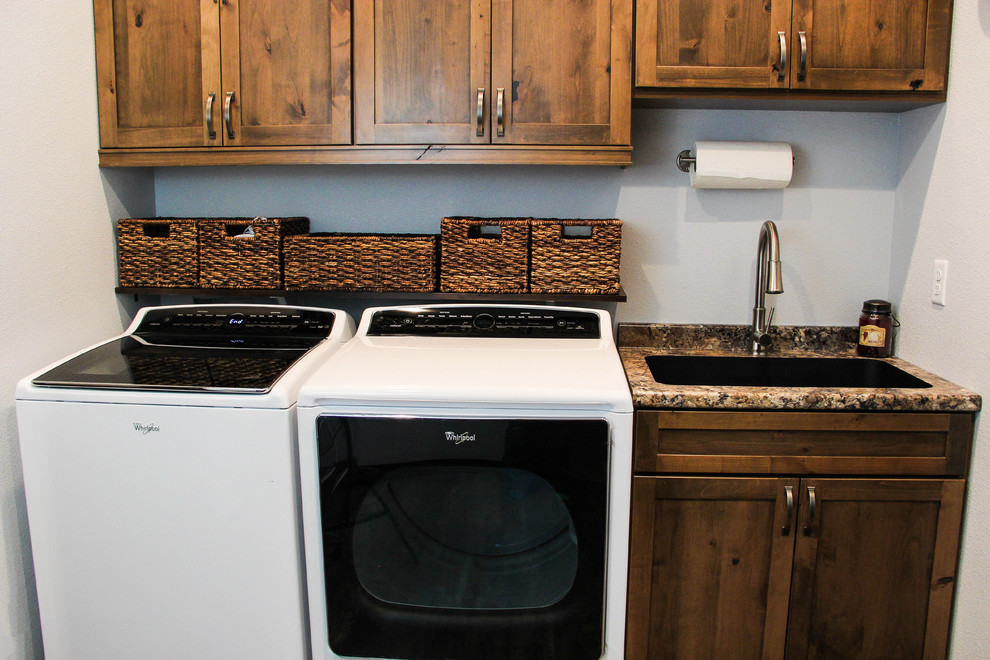 Mid-sized country single-wall dedicated laundry room in Other with an undermount sink, recessed-panel cabinets, medium wood cabinets, granite benchtops, grey walls and a side-by-side washer and dryer.