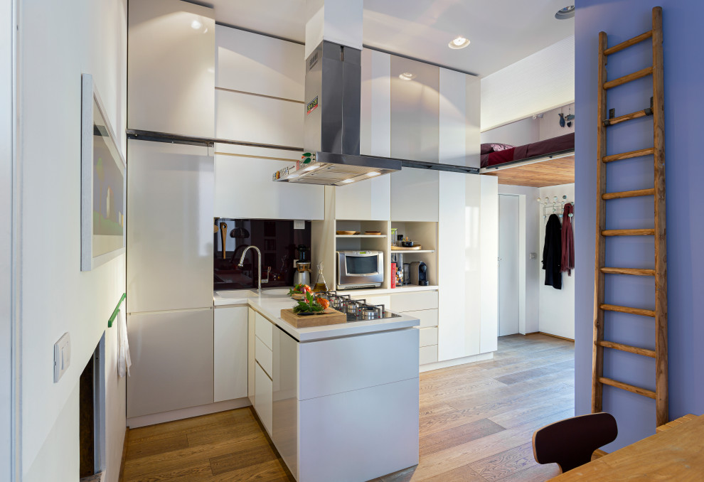 This is an example of a small contemporary single-wall kitchen/diner in Milan with an integrated sink, flat-panel cabinets, white cabinets, composite countertops, red splashback, glass sheet splashback, stainless steel appliances, medium hardwood flooring, a breakfast bar, beige floors, white worktops and a drop ceiling.