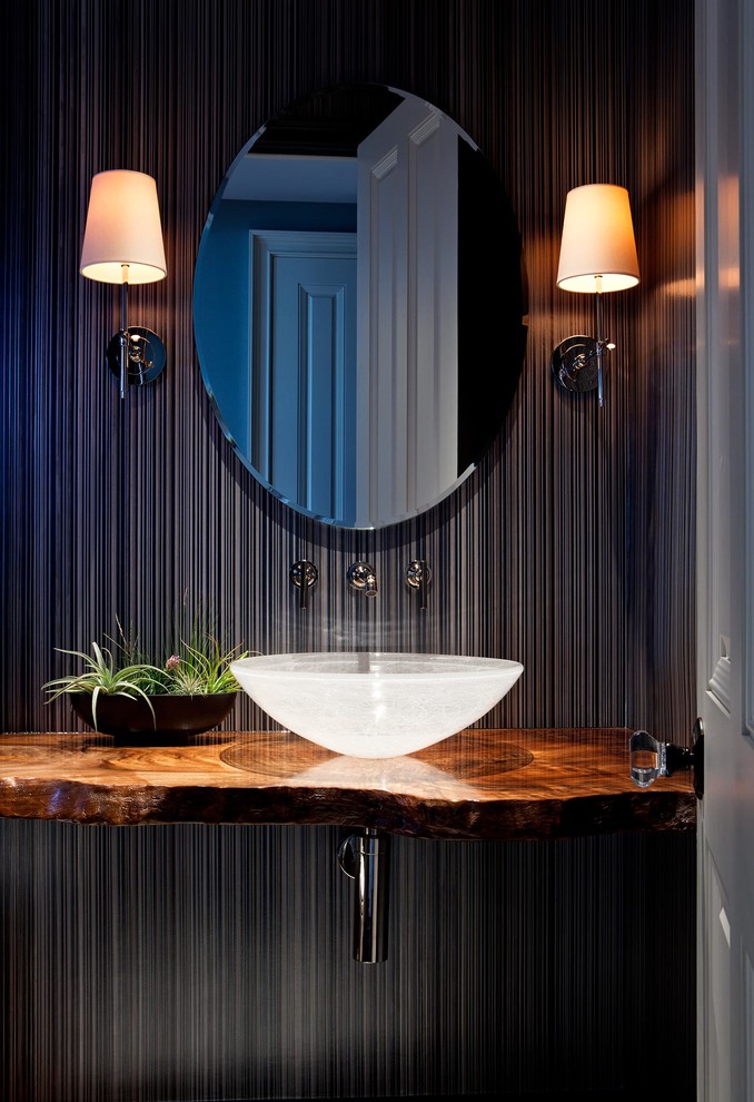Photo of a tropical powder room in San Francisco with a vessel sink, black walls and brown benchtops.
