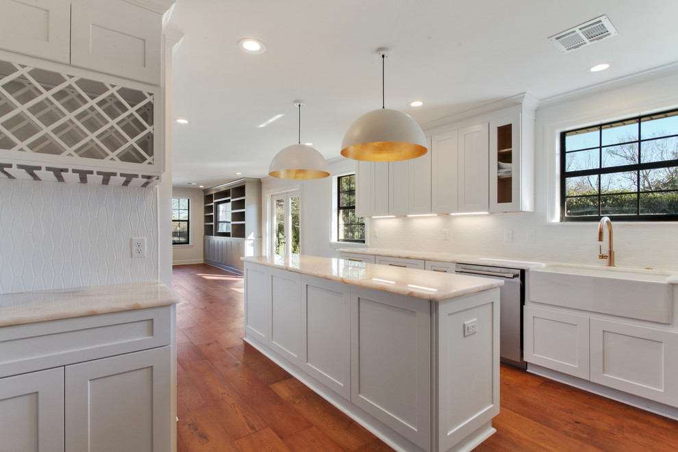 Mid-sized transitional l-shaped eat-in kitchen in New Orleans with a farmhouse sink, shaker cabinets, grey cabinets, quartz benchtops, white splashback, ceramic splashback, stainless steel appliances, medium hardwood floors, with island, brown floor and multi-coloured benchtop.