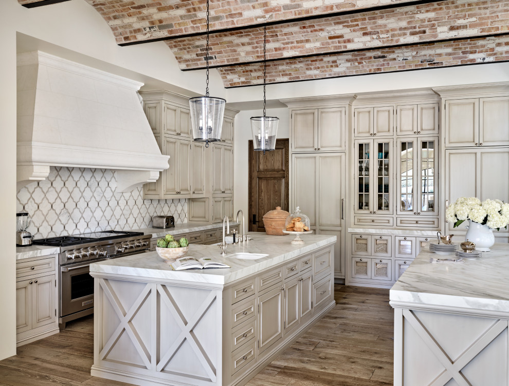 Inspiration for a mediterranean u-shaped eat-in kitchen in Phoenix with a farmhouse sink, recessed-panel cabinets, beige cabinets, grey splashback, panelled appliances, medium hardwood floors, multiple islands, brown floor, grey benchtop and vaulted.