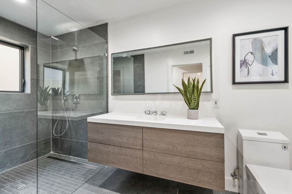 Photo of a large contemporary 3/4 bathroom in San Francisco with light wood cabinets, an open shower, gray tile, porcelain tile, white walls, porcelain floors, an integrated sink, engineered quartz benchtops, grey floor, white benchtops, flat-panel cabinets, a two-piece toilet and an open shower.