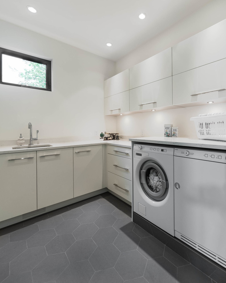 Photo of a mid-sized midcentury l-shaped dedicated laundry room in Vancouver with an undermount sink, flat-panel cabinets, white cabinets, quartz benchtops, white walls, ceramic floors, a side-by-side washer and dryer and grey floor.
