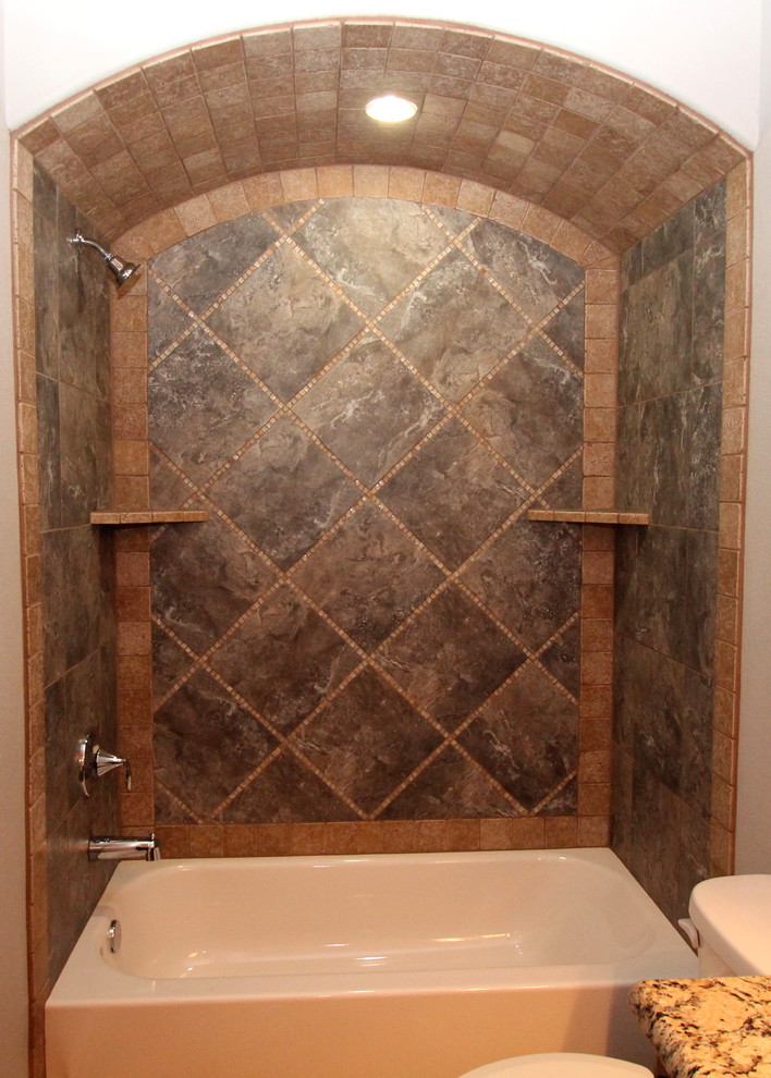 Photo of a large transitional 3/4 bathroom in Dallas with raised-panel cabinets, medium wood cabinets, a drop-in tub, a shower/bathtub combo, a two-piece toilet, gray tile, ceramic tile, grey walls and concrete floors.