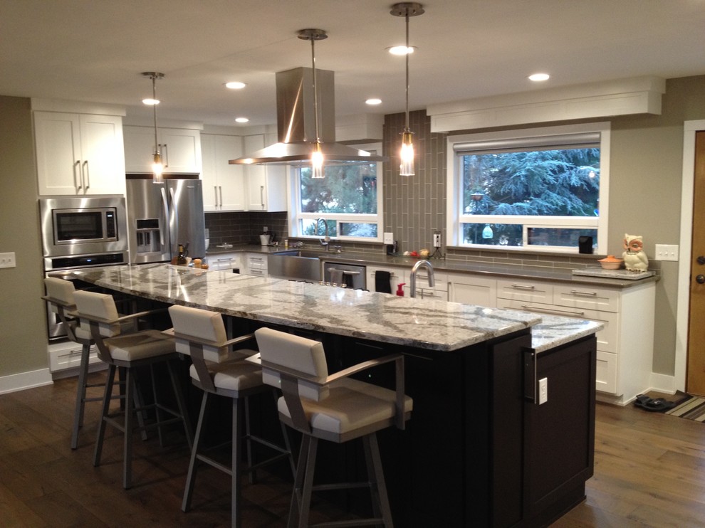 Photo of a large contemporary u-shaped eat-in kitchen in Boise with a farmhouse sink, shaker cabinets, white cabinets, quartz benchtops, grey splashback, glass tile splashback, stainless steel appliances, medium hardwood floors and with island.