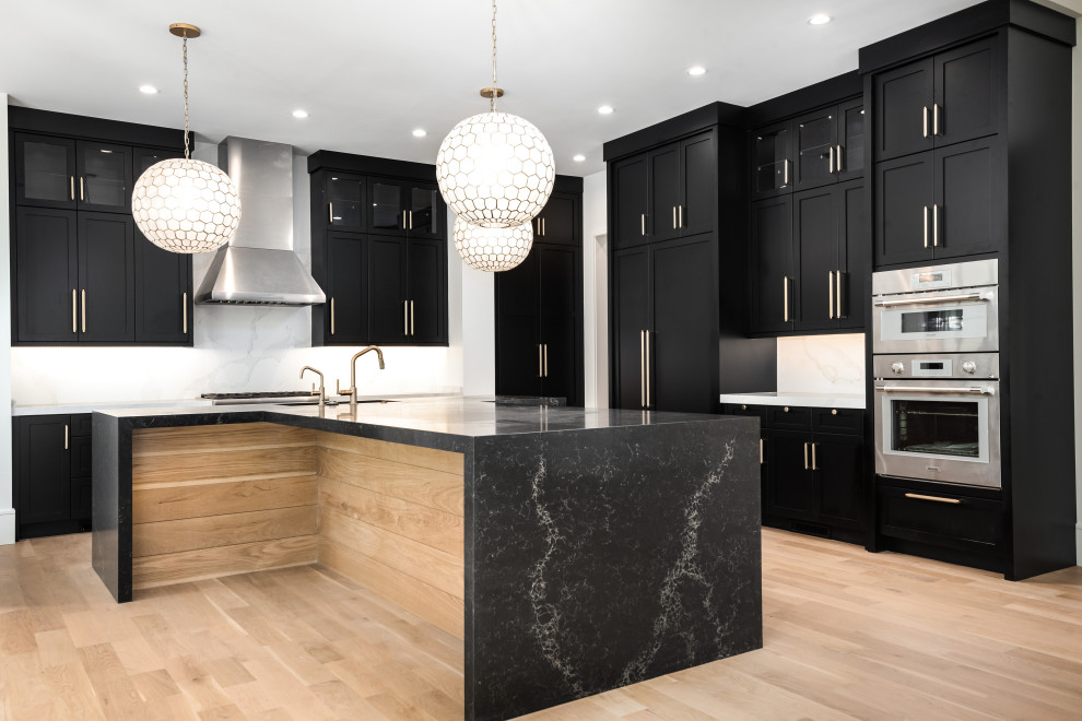 Inspiration for a mid-sized transitional u-shaped light wood floor kitchen remodel with an undermount sink, shaker cabinets, black cabinets, quartz countertops, white backsplash, quartz backsplash, stainless steel appliances, an island and black countertops