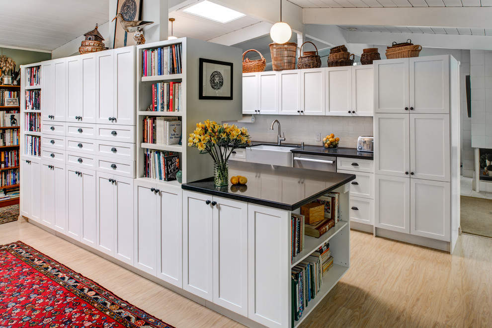 Photo of a small arts and crafts galley kitchen pantry in San Francisco with a farmhouse sink, shaker cabinets, white cabinets, solid surface benchtops, white splashback, porcelain splashback, stainless steel appliances, light hardwood floors and with island.