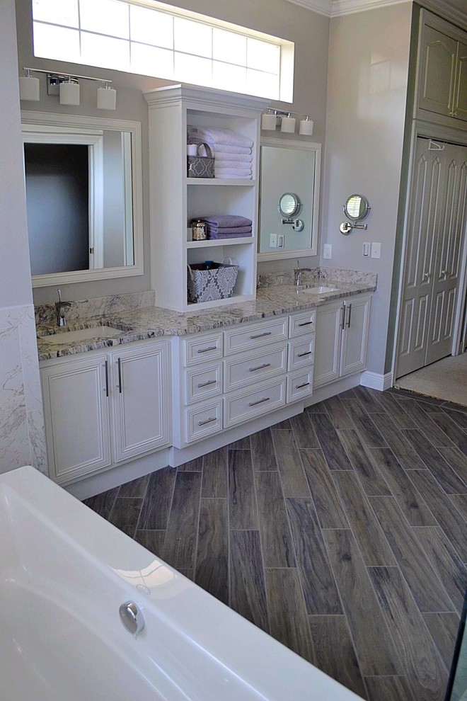 Large transitional master laminate floor and brown floor alcove bathtub photo with recessed-panel cabinets, white cabinets, beige walls, an undermount sink, quartz countertops and white countertops
