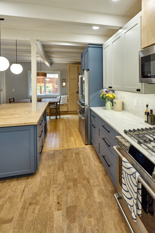 Eklektisk inredning av ett vit vitt kök och matrum, med en enkel diskho, skåp i shakerstil, blå skåp, bänkskiva i kvarts, grått stänkskydd, stänkskydd i keramik, rostfria vitvaror, korkgolv, en köksö och beiget golv