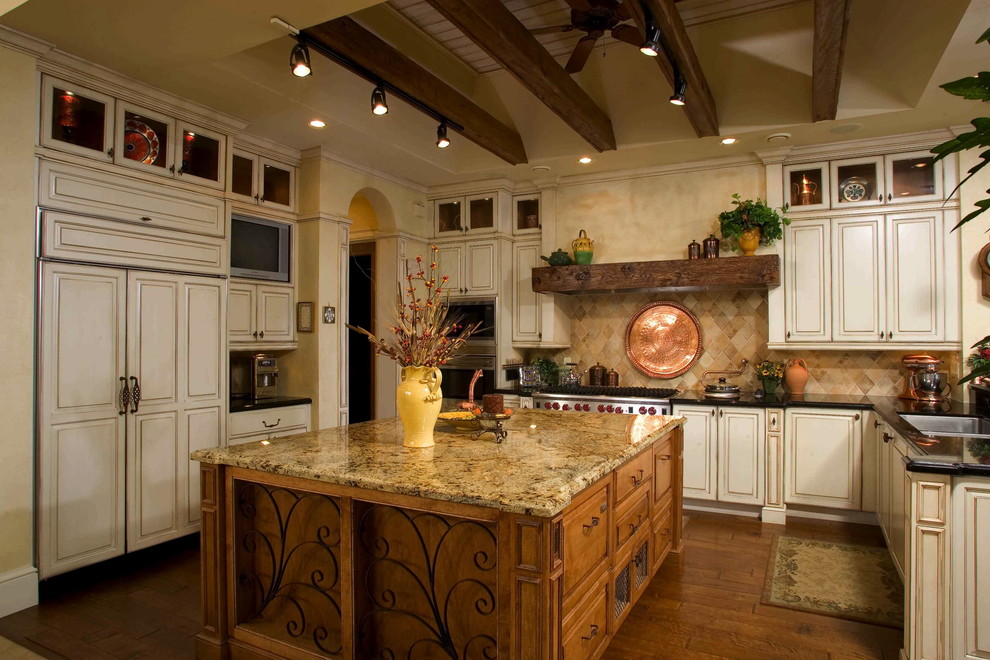 This is an example of a large mediterranean galley eat-in kitchen in San Francisco with a drop-in sink, flat-panel cabinets, beige cabinets, granite benchtops, beige splashback, stainless steel appliances, medium hardwood floors, with island, brown floor and black benchtop.